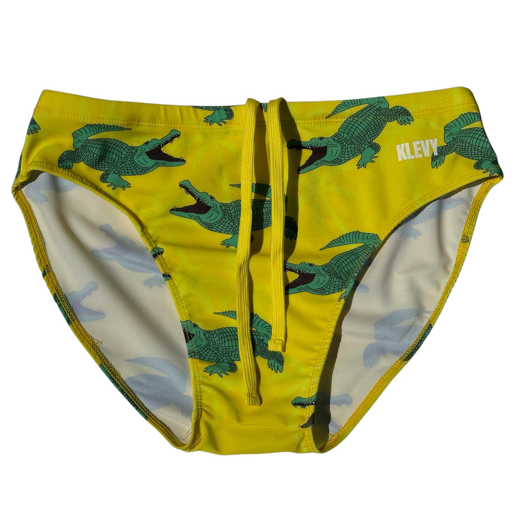 Yellow swim briefs with green crocodile pattern on a white background