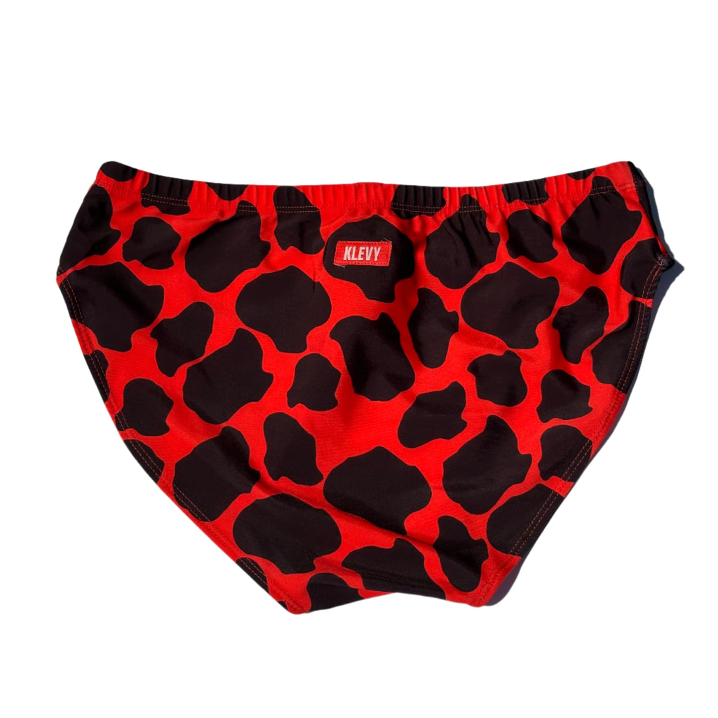Red swim briefs with black cow print pattern on a white background